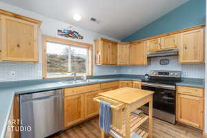 Kitchen featuring light wood finish cabinets, stainless steel appliances, lofted ceiling, backsplash, and light wood-type flooring