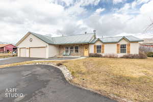 Ranch-style house with driveway, stone siding, an attached garage, a metal roof, and a front yard