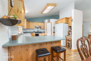 Kitchen featuring lofted ceiling, a peninsula, white fridge with ice dispenser, decorative backsplash, and stainless steel range with electric stovetop