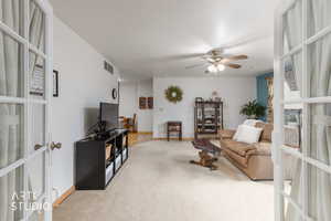 Living room with a ceiling fan, light colored carpet, and french doors