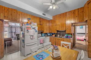 Kitchen with white appliances, wood finish cabinets, ceiling fan, tasteful backsplash, and wooden walls