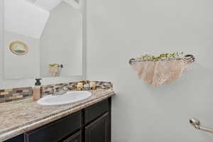 Bathroom featuring vanity, lofted ceiling, and backsplash