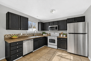 Virtually Staged Kitchen featuring dark cabinetry, laminate countertops, tile backsplash, stainless steel appliances, and tile flooring