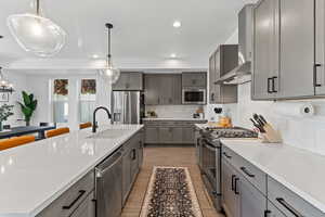 Kitchen featuring stainless steel appliances, recessed lighting, decorative light fixtures, light wood-style flooring, and wall chimney exhaust hood
