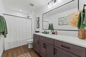 Full bath with a textured ceiling, vanity, dark wood finished floors, shower / bathtub combination with curtain, and recessed lighting