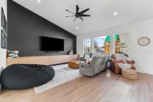 Living area featuring wood walls, wood finished floors, recessed lighting, a ceiling fan, and an accent wall