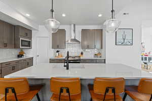 Kitchen featuring a kitchen bar, hanging light fixtures, backsplash, wall chimney exhaust hood, and appliances with stainless steel finishes