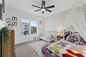 Carpeted bedroom featuring wallpapered walls, a nursery area, and ceiling fan