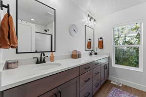 Bathroom featuring dark wood-style floors, double vanity, a stall shower, and a textured ceiling