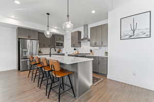 Kitchen featuring gray cabinetry, stainless steel appliances, decorative light fixtures, a breakfast bar, and a center island with sink