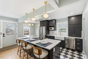 Kitchen with stainless steel appliances, a kitchen bar, a center island, dark cabinets, and light stone counters