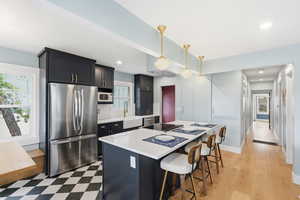 Kitchen with stainless steel appliances, a center island, a breakfast bar area, hanging light fixtures, and dark cabinets