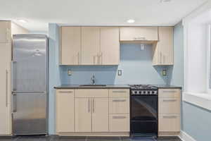 Kitchen featuring black stove, stainless steel fridge, dark stone countertops, light wood finish cabinets, and recessed lighting