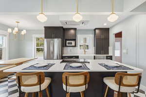 Kitchen with a breakfast bar, stainless steel appliances, a kitchen island, decorative light fixtures, and exhaust hood