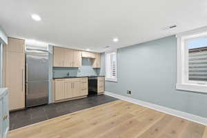Kitchen with stainless steel built in refrigerator, light wood finish cabinetry, dark wood-type flooring, dark countertops, and dishwasher