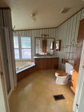 Full bath with double vanity, a garden tub, light flooring, and wallpapered walls