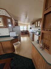 Kitchen featuring wood finish cabinetry, light flooring, glass fronted cabinets, and white appliances