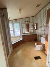 Full bathroom with double vanity, a garden tub, light flooring, wallpapered walls, and a textured ceiling