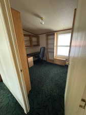 Office space with built in desk, dark colored carpet, and a textured ceiling