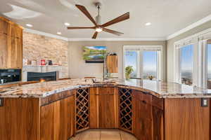 Kitchen with wood finish cabinets, light stone countertops, a large fireplace, crown molding, and recessed lighting