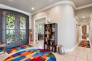 Foyer entrance with arched walkways, french doors, ornamental molding, light tile patterned flooring, and beverage cooler