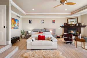 Bedroom featuring a tray ceiling, a ceiling fan, a glass covered fireplace, wood finished floors, and recessed lighting