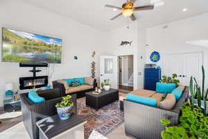 Living area with a ceiling fan, a glass covered fireplace, light tile patterned floors, and vaulted ceiling