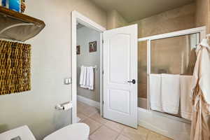 Bathroom with enclosed tub / shower combo and light tile patterned floors