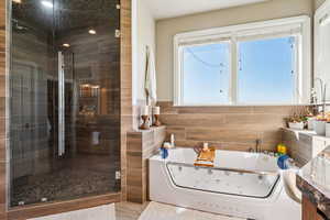 Full bath featuring a whirlpool tub, a stall shower, and tile walls