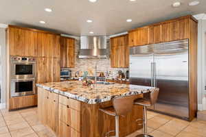 Kitchen featuring light stone counters, stainless steel appliances, a kitchen bar, decorative backsplash, and an island with sink