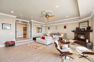 Living room featuring ornamental molding, wood finished floors, a glass covered fireplace, a ceiling fan, and recessed lighting