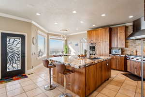 Kitchen with crown molding, wood finish cabinets, light stone countertops, a kitchen island with sink, and a kitchen breakfast bar