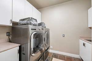 Laundry area featuring cabinet space, washer and clothes dryer, and dark stone finish floors