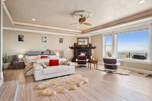Living area with a ceiling fan, light wood-style flooring, a tray ceiling, a glass covered fireplace, and recessed lighting
