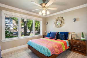Bedroom featuring light wood-style floors, crown molding, and a ceiling fan