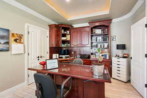 Office space featuring crown molding, light wood-style flooring, a raised ceiling, and built in study area