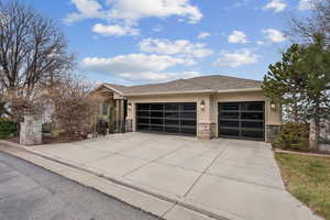 View of front of house with stone siding, a shingled roof, concrete driveway, a garage, and stucco siding