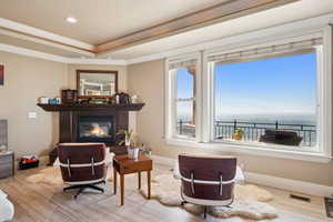 Living room with light wood finished floors, a glass covered fireplace, a tray ceiling, ornamental molding, and recessed lighting