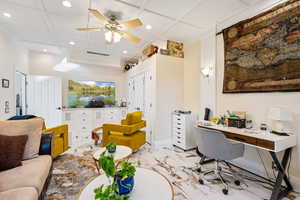 Home office featuring coffered ceiling, recessed lighting, light marble finish floors, and a ceiling fan