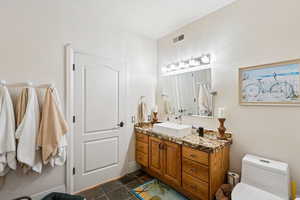 Full bath with vanity, a textured wall, and dark tile patterned floors