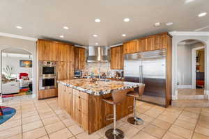 Kitchen with arched walkways, stainless steel appliances, light stone countertops, wood finish cabinetry, and recessed lighting