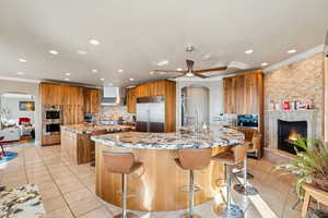 Kitchen featuring arched walkways, light stone counters, a kitchen bar, backsplash, and crown molding