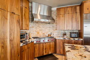 Kitchen featuring dark stone countertops, range hood, wood finish cabinets, and stainless steel appliances