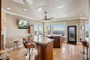 Kitchen featuring a textured ceiling, light stone countertops, light tile patterned floors, a center island with sink, and recessed lighting
