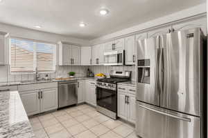 Kitchen with stainless steel appliances, light stone countertops, recessed lighting, light tile patterned flooring, and decorative backsplash