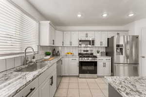 Kitchen with stainless steel appliances, light stone counters, white cabinetry, light tile patterned flooring, and recessed lighting