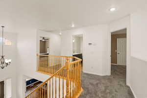 Corridor featuring an upstairs landing, carpet, hanging lights, and a textured ceiling