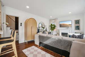 Living area with arched walkways, ornamental molding, dark wood-type flooring, a glass covered fireplace, and recessed lighting