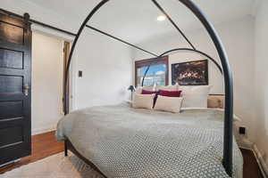 Bedroom featuring a barn door, wood finished floors, ornamental molding, and recessed lighting