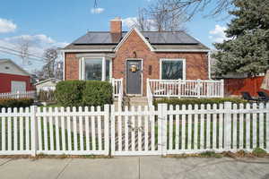Bungalow-style home featuring brick siding, a chimney, solar panels, and a fenced front yard
